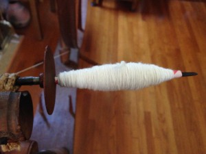 Singles on a driven spindle wheel. A paper straw quill was used on the spindle to hold the spun singles yarn.