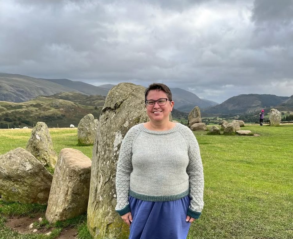 Karen in a handknit sweater in a field with standing stones and sheep in northern England