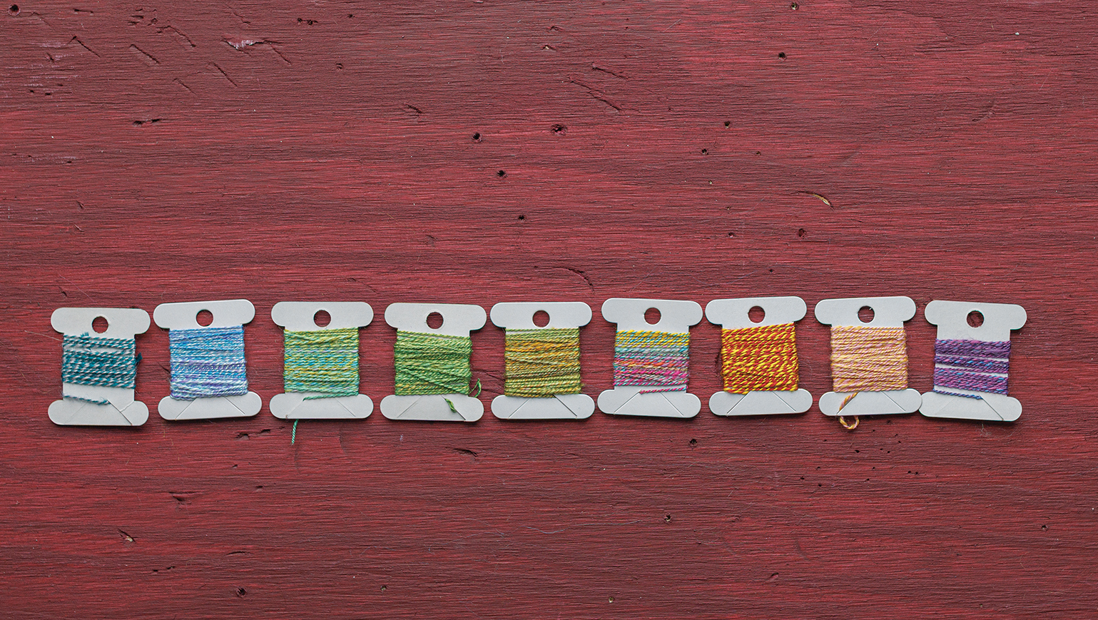A row of tiny bobbins of handspun in a rainbow of colors